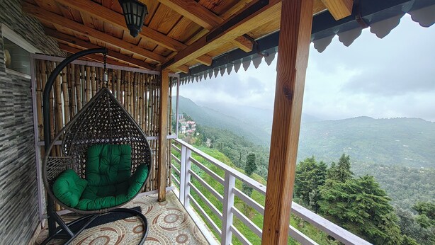 Un balcón de madera con una hamaca colgante y vistas a un paisaje montañoso.