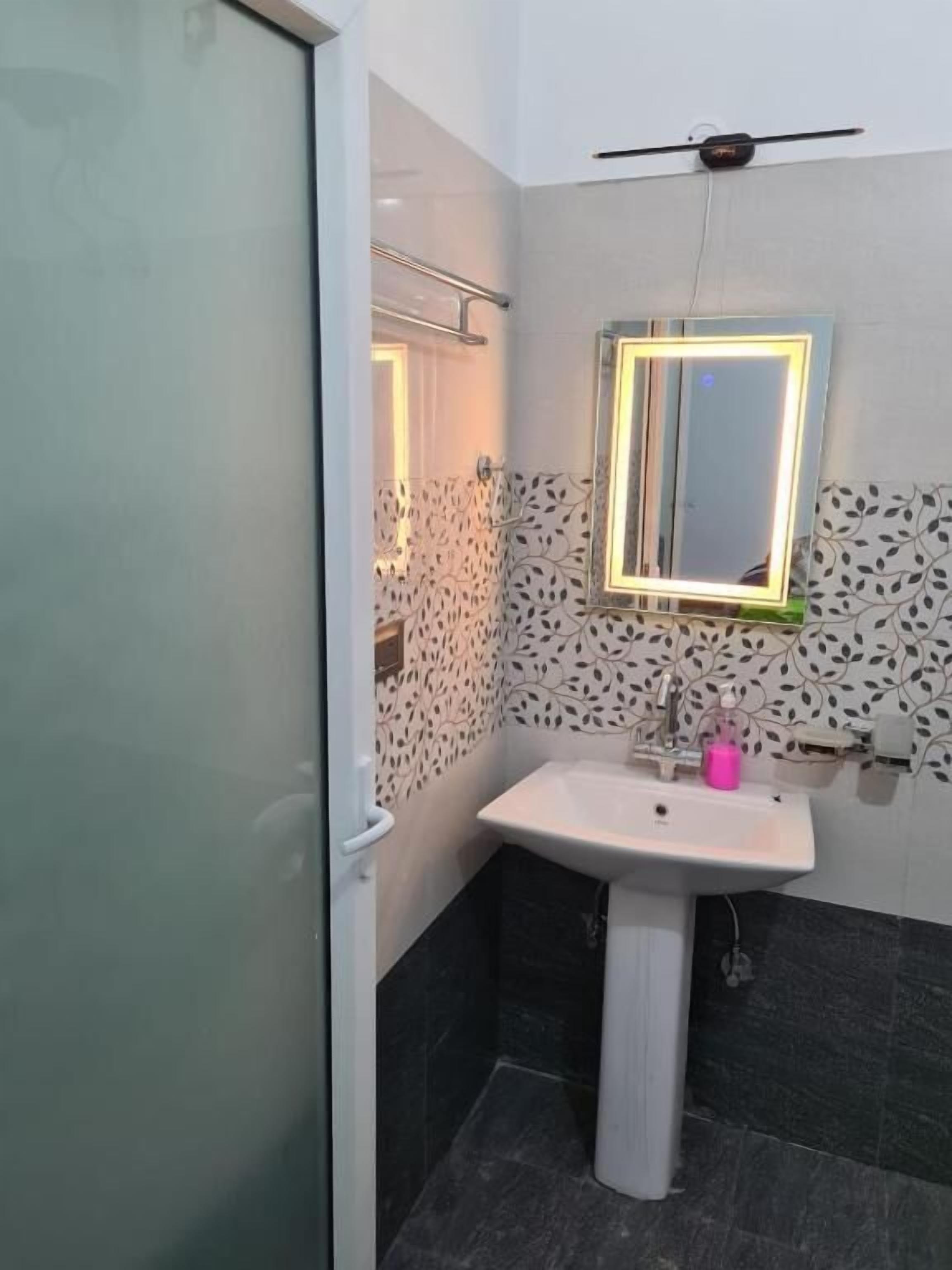 A bathroom with a white sink, a mirror with a light, and patterned wall tiles.