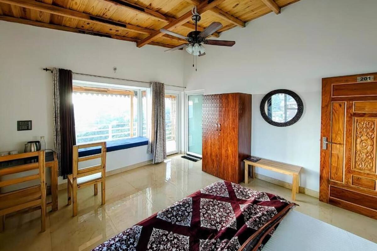 Une pièce avec un ventilateur de plafond, un lit recouvert d’une courtepointe à motifs, une armoire en bois et une fenêtre avec des rideaux.