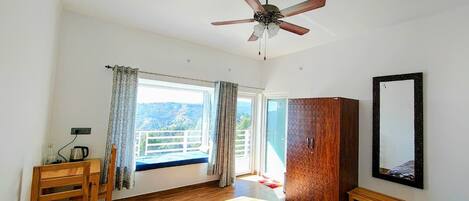 Un dormitorio con cama, ventilador de techo, armario de madera, un banco, ventana con cortinas y vistas al exterior.