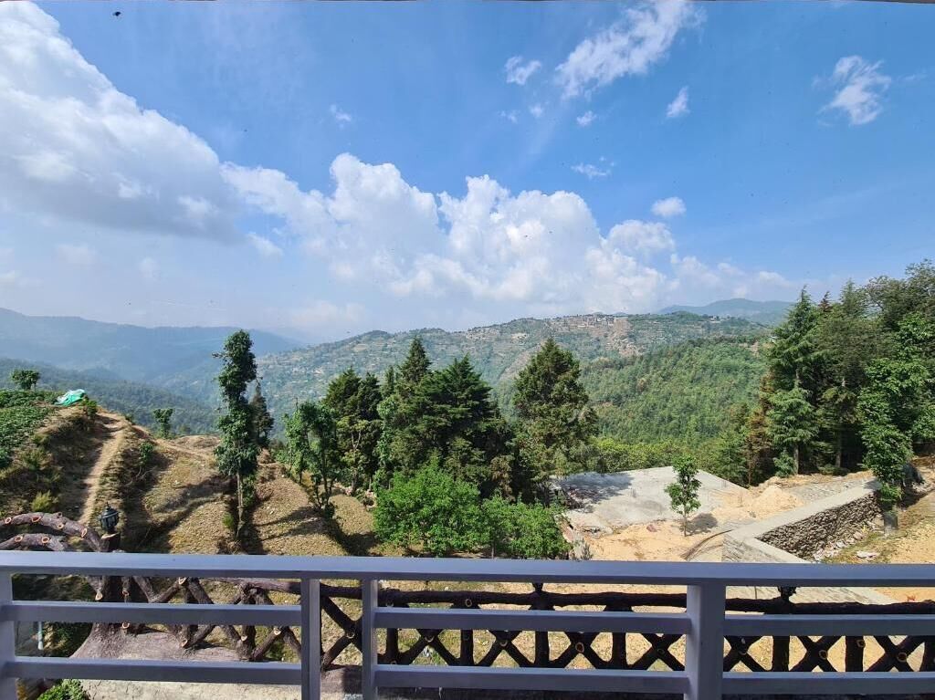 Un paisaje montañoso con cielo despejado, una valla de madera en primer plano y un pueblo lejano.