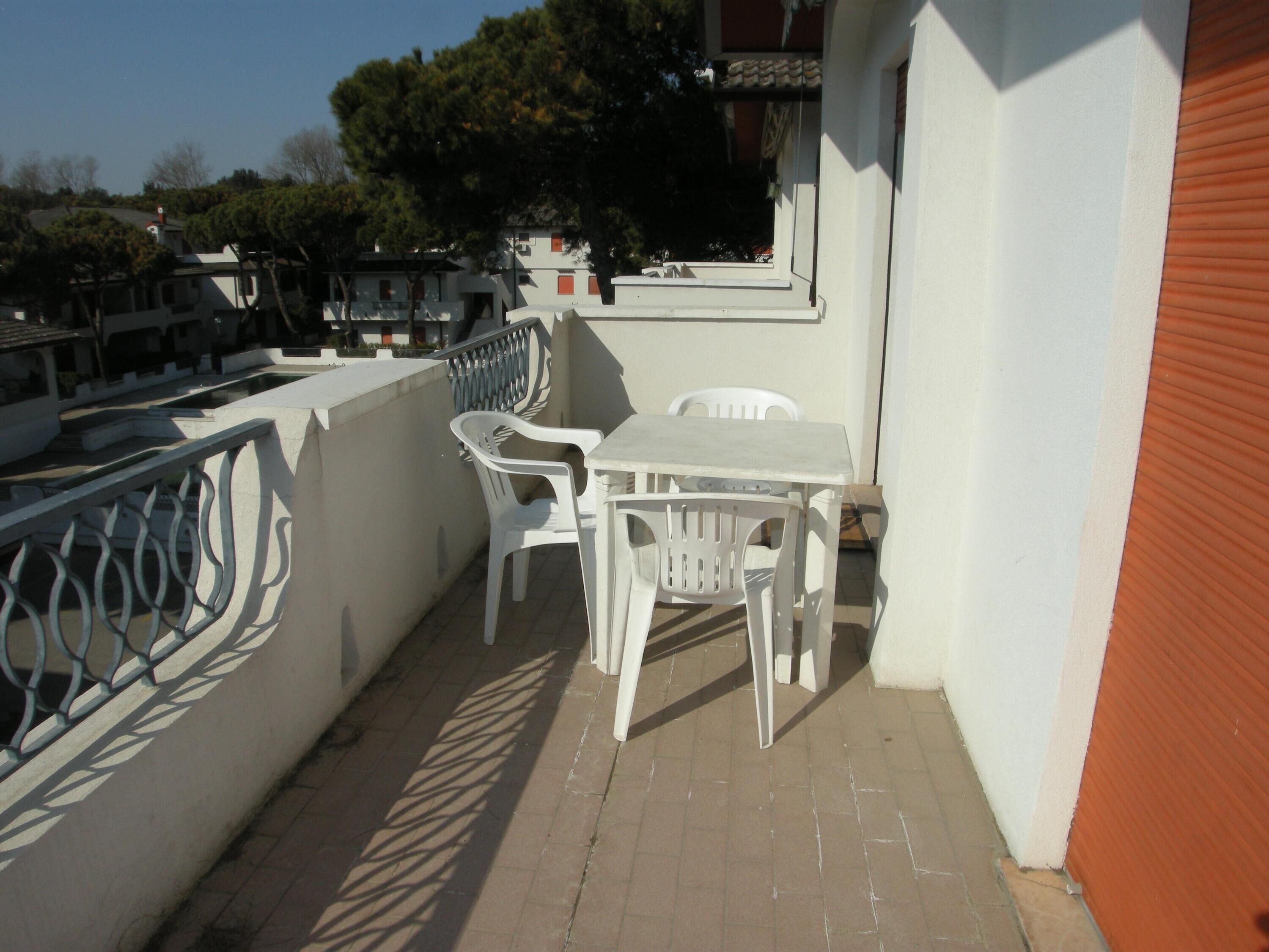 A balcony with a table and chairs, a railing, and a view of the surrounding area.