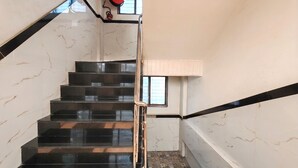 A staircase with black steps and a metal handrail, leading to a landing with a window and a red object on the wall.