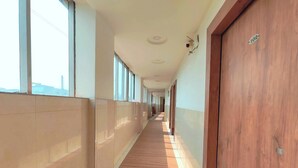 A long, narrow hallway with wooden flooring, large windows, and doors on one side.