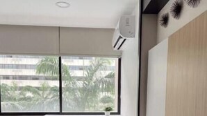 Ein modernes Schlafzimmer mit großem Fenster, einem Bett mit vielen Kissen, einem Heizkörper und einer Wand-Klimaanlage.