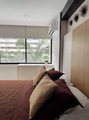 Ein modernes Schlafzimmer mit großem Fenster, einem Bett mit vielen Kissen, einem Heizkörper und einer Wand-Klimaanlage.