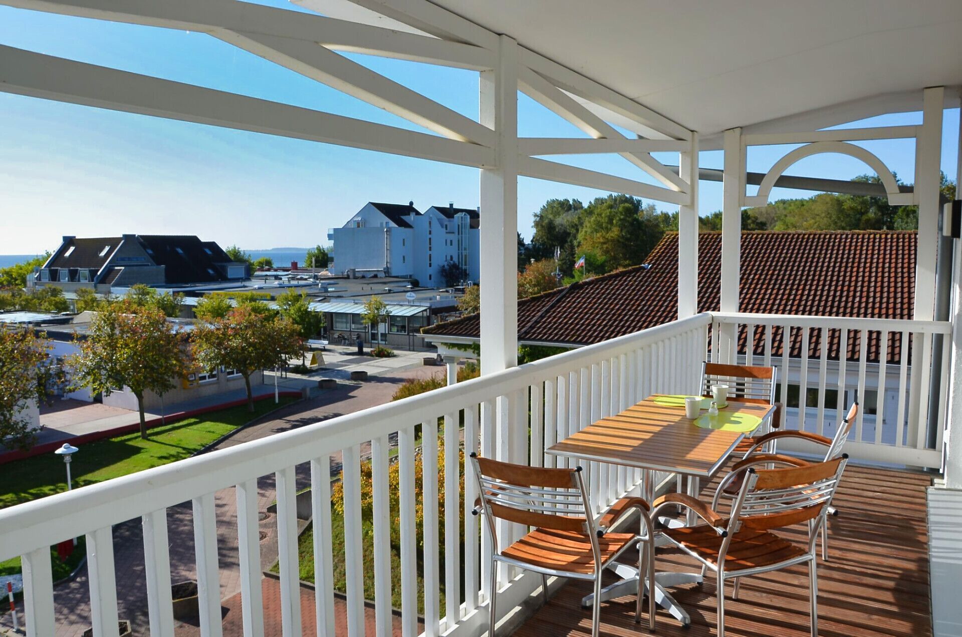 Ein Balkon mit Tisch und Stühlen, mit Blick auf ein Wohngebiet mit Häusern und einem klaren Himmel.