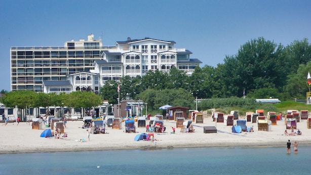 Un hotel frente a la playa con varios balcones, una playa de arena y carpas a la orilla del mar.