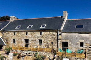 Un bâtiment en pierre doté de nombreuses fenêtres, une clôture en bois et un ciel d’un bleu éclatant.