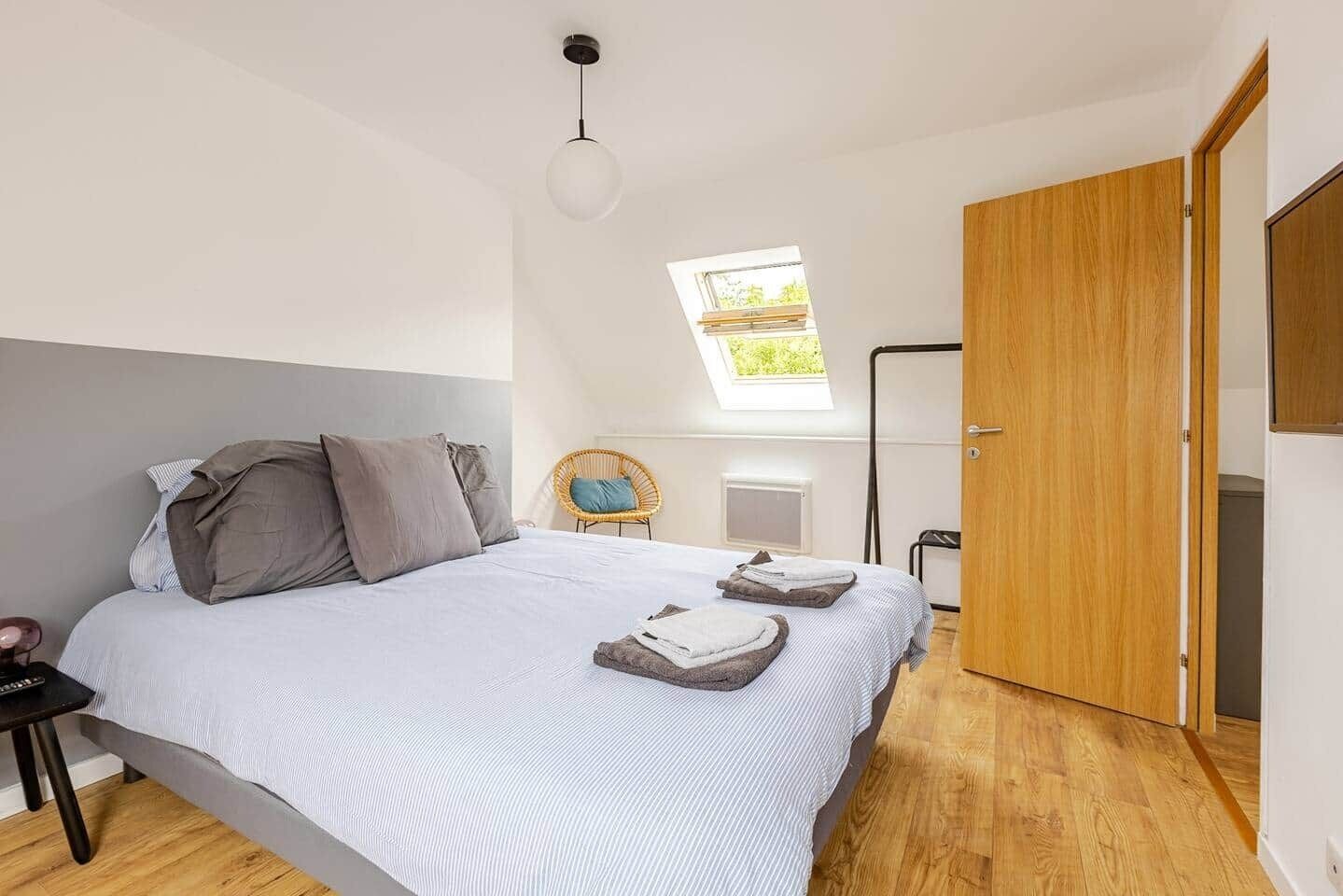 A bedroom with a bed, a chair, a skylight, and a wooden door.
