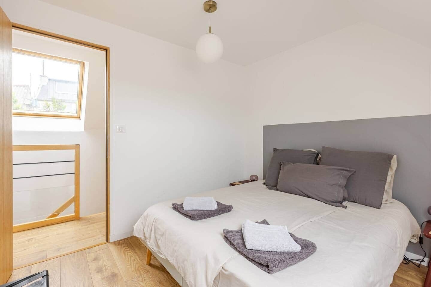 A bedroom with a bed, two pillows, a bedside table, a lamp, and a window.