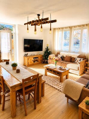 Ein gemütliches Wohnzimmer mit Esstisch aus Holz, einer Couch und einem Fernseher.