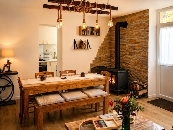 Ein gemütliches Wohnzimmer mit einem Holzesstisch, gepolsterten Bänken, einem Kamin und einer Küche im Hintergrund.
