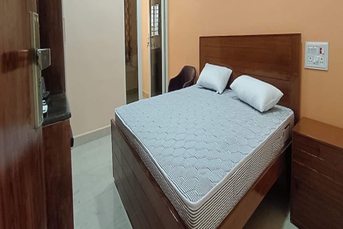 A bedroom with a bed, a wooden headboard, a nightstand, a wardrobe, and an air conditioning unit.