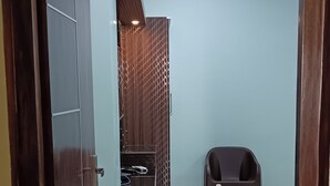 Ein Zimmer mit Fliesenboden, einer Holztür mit Schild und einem Plastikstuhl sowie einem kleinen Tisch mit einer Dekoration.