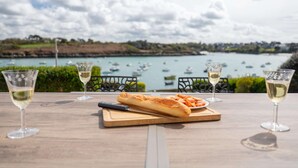 Un tavolo con bicchieri da vino e una baguette, affacciato su un porto con barche.