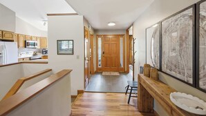 A kitchen with wooden cabinets, a microwave, and a stove. There is a wooden bench with a white tray and a framed artwork on the wall. - Loveland Luxury Getaway | Pool | Golf Course (Loveland)