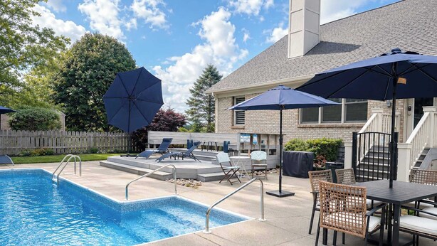 A swimming pool with lounge chairs and umbrellas, a fire pit, and a brick building in the background. - Loveland Luxury Getaway | Pool | Golf Course (Loveland)