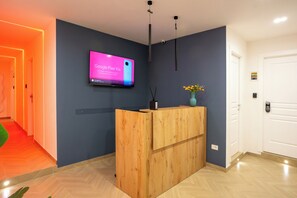 Ein Empfangsschalter mit montiertem Fernseher, der eine Werbung zeigt, eine Holztresen, eine Vase mit Blumen und eine Tür mit Zahlenschloss.