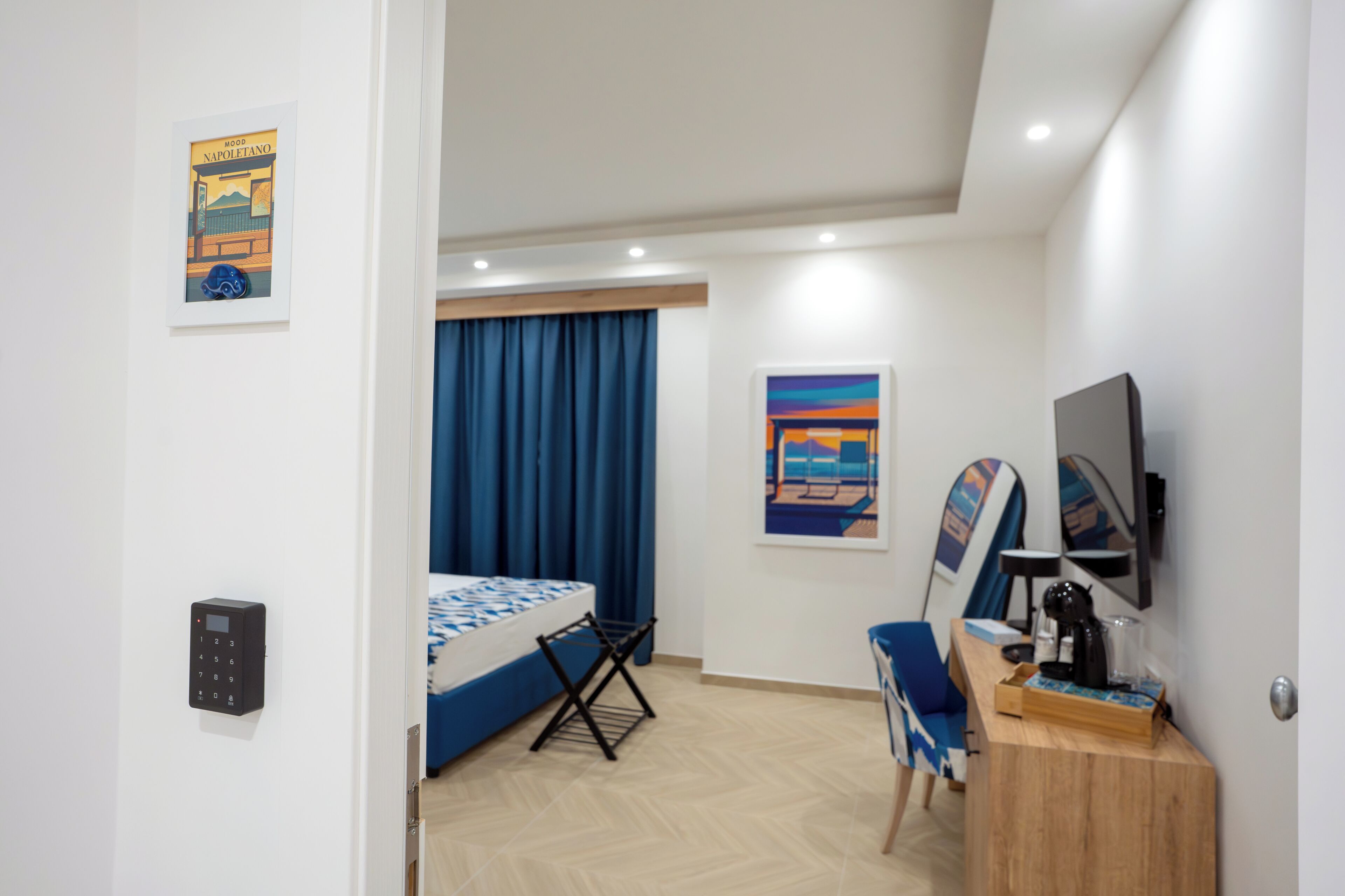 A hotel room with a bed, a desk, a chair, a TV, a painting, and a window with curtains.
