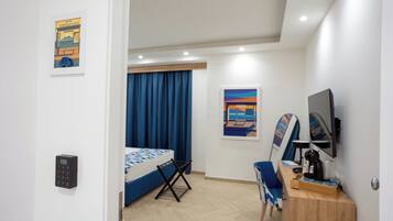 A hotel room with a bed, a desk, a chair, a TV, a painting, and a window with curtains.