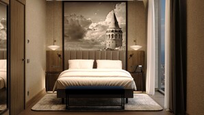 A modern hotel room with a large bed, a cityscape mural on the wall, and a view of the city through the window.