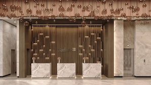 A modern reception area with marble counters, a wooden panel wall, and a ceiling with hanging spherical lights.