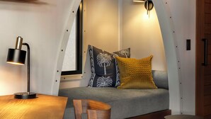 Un plafond en arc de cercle, un canapé avec des coussins à motifs, une table avec une lampe et une étagère avec des tasses.