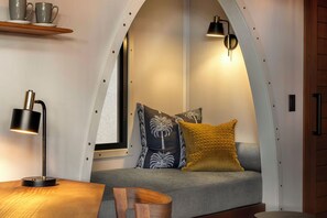 Un soffitto ad arco, un divano con cuscini decorati, un tavolo con una lampada e uno scaffale con tazze.