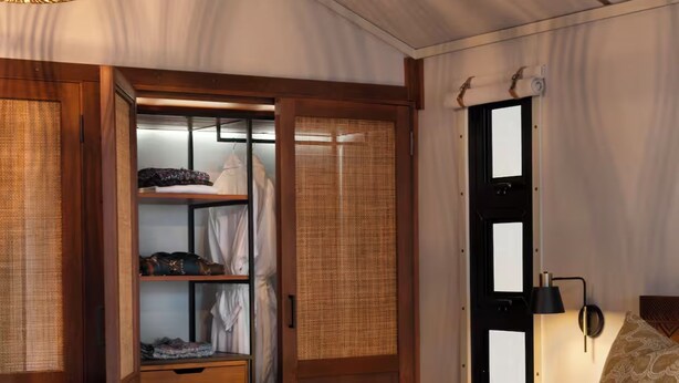 Une pièce avec une armoire en bois, un lit recouvert d’une couvre-lit à motifs et une lampe fixée au mur.