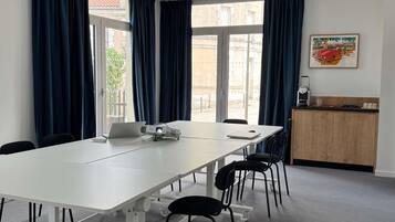A conference room with a long table, chairs, a projector, a laptop, and a small kitchenette area.