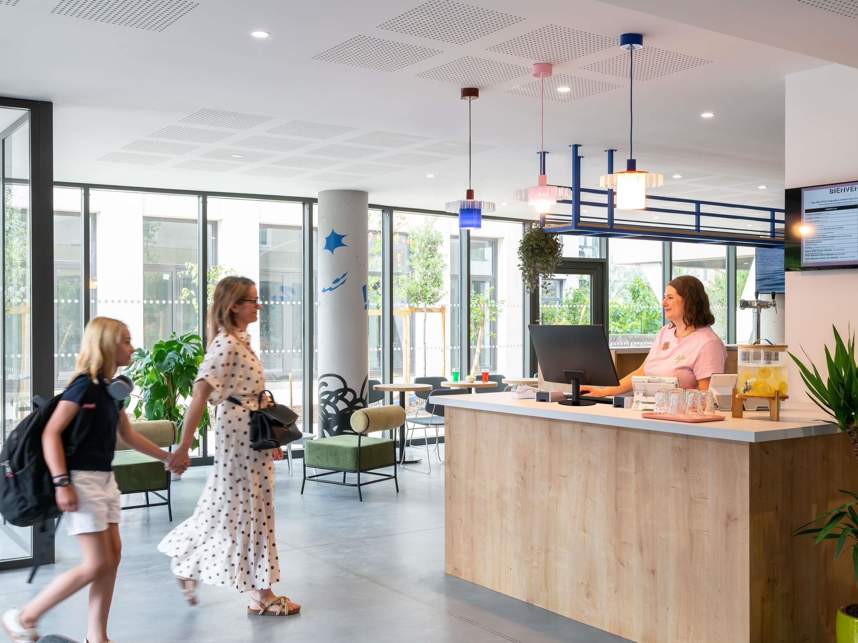 Una zona reception con un bancone in legno, una receptionist e un'ampia finestra vista all'esterno.