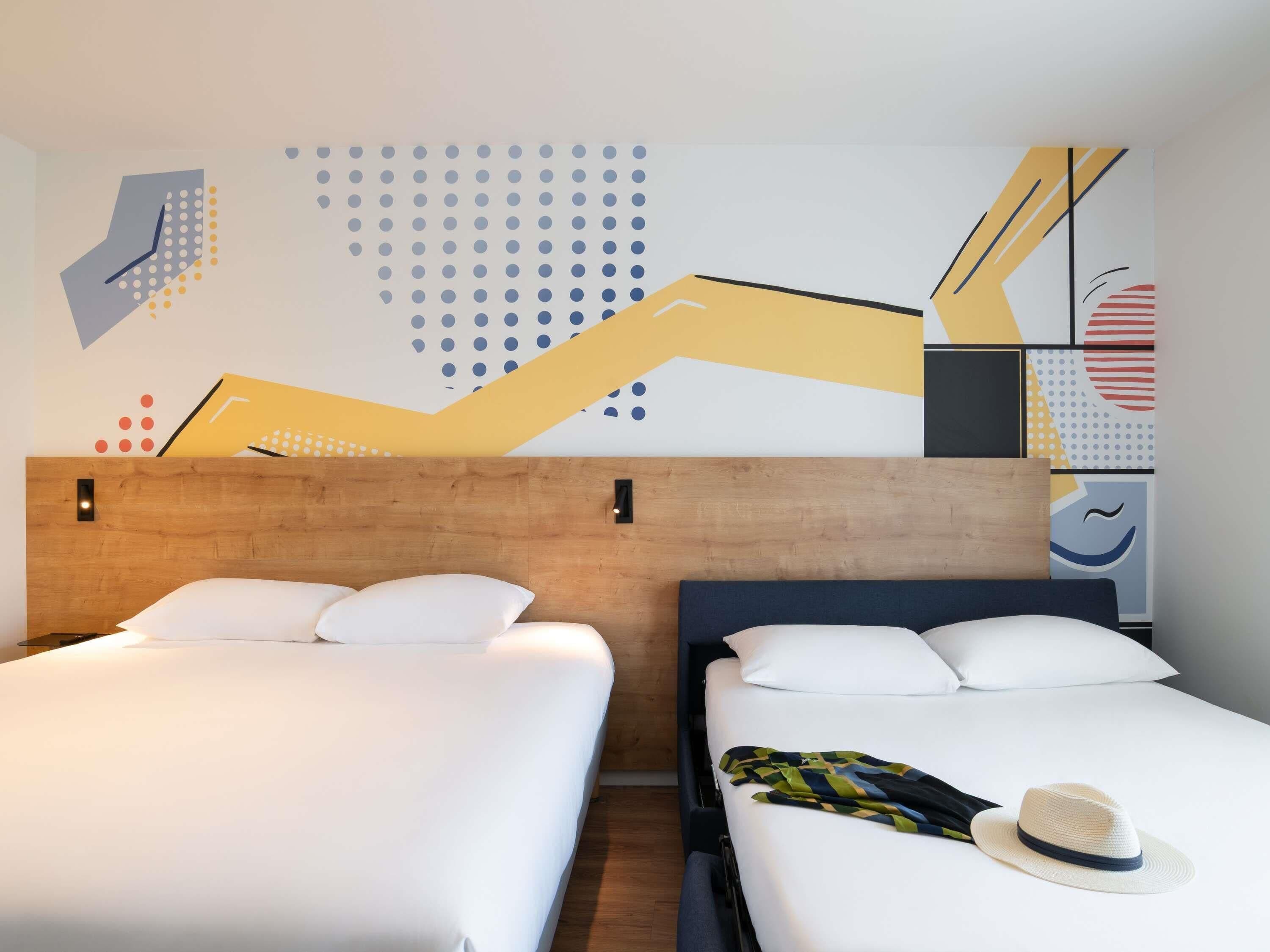 A hotel room with two beds, a wooden headboard, and a wall with abstract art.