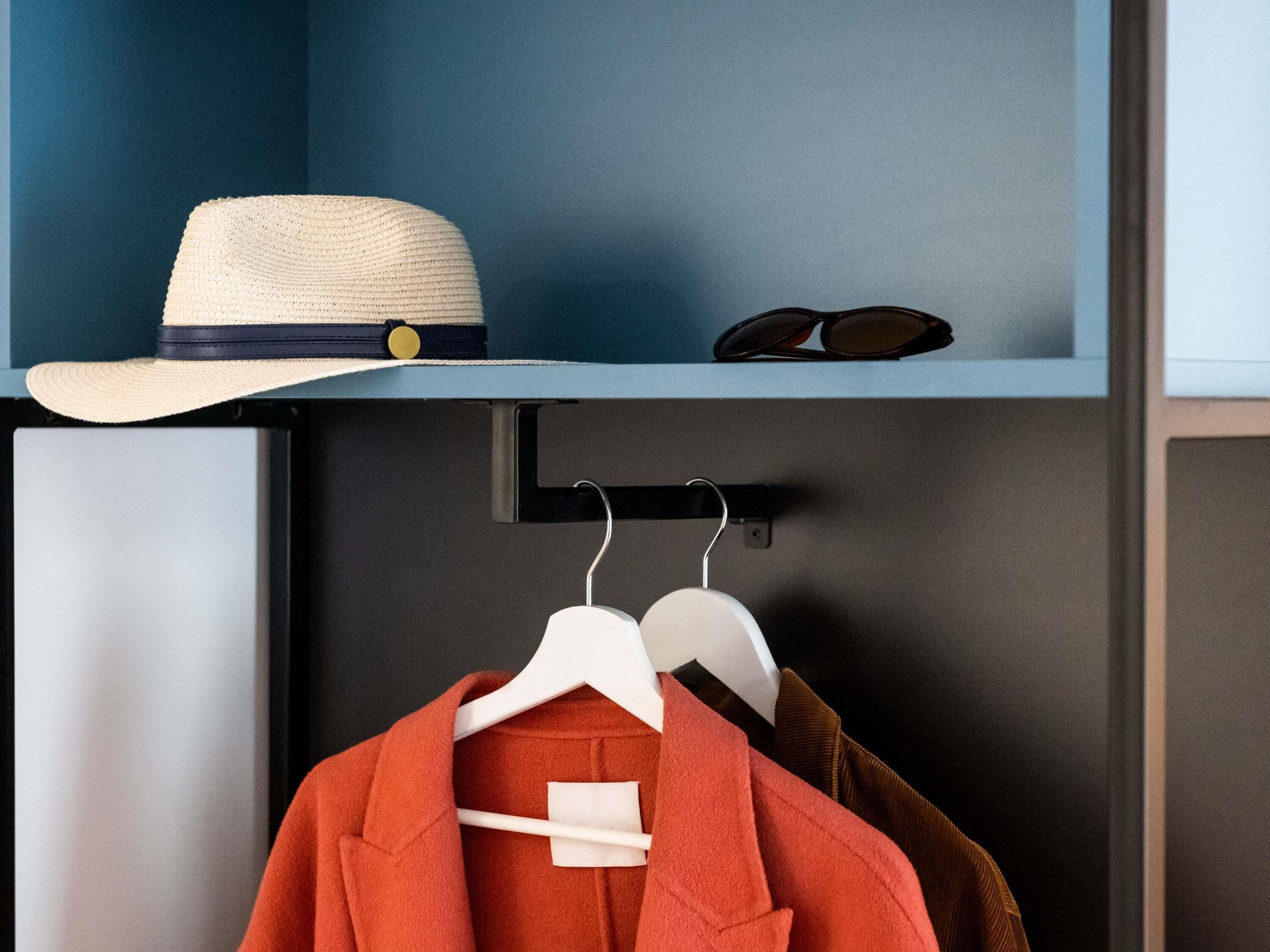 A room with a blue wall, a hat on a shelf, and a coat on a hanger.