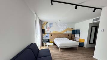 Una habitación de hotel moderna con una cama, un sofá, una mesita y una silla.