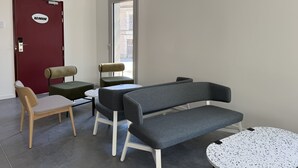 Uma área de espera moderna com uma porta vermelha identificada com 'REUNION', uma pequena mesa redonda e duas cadeiras.