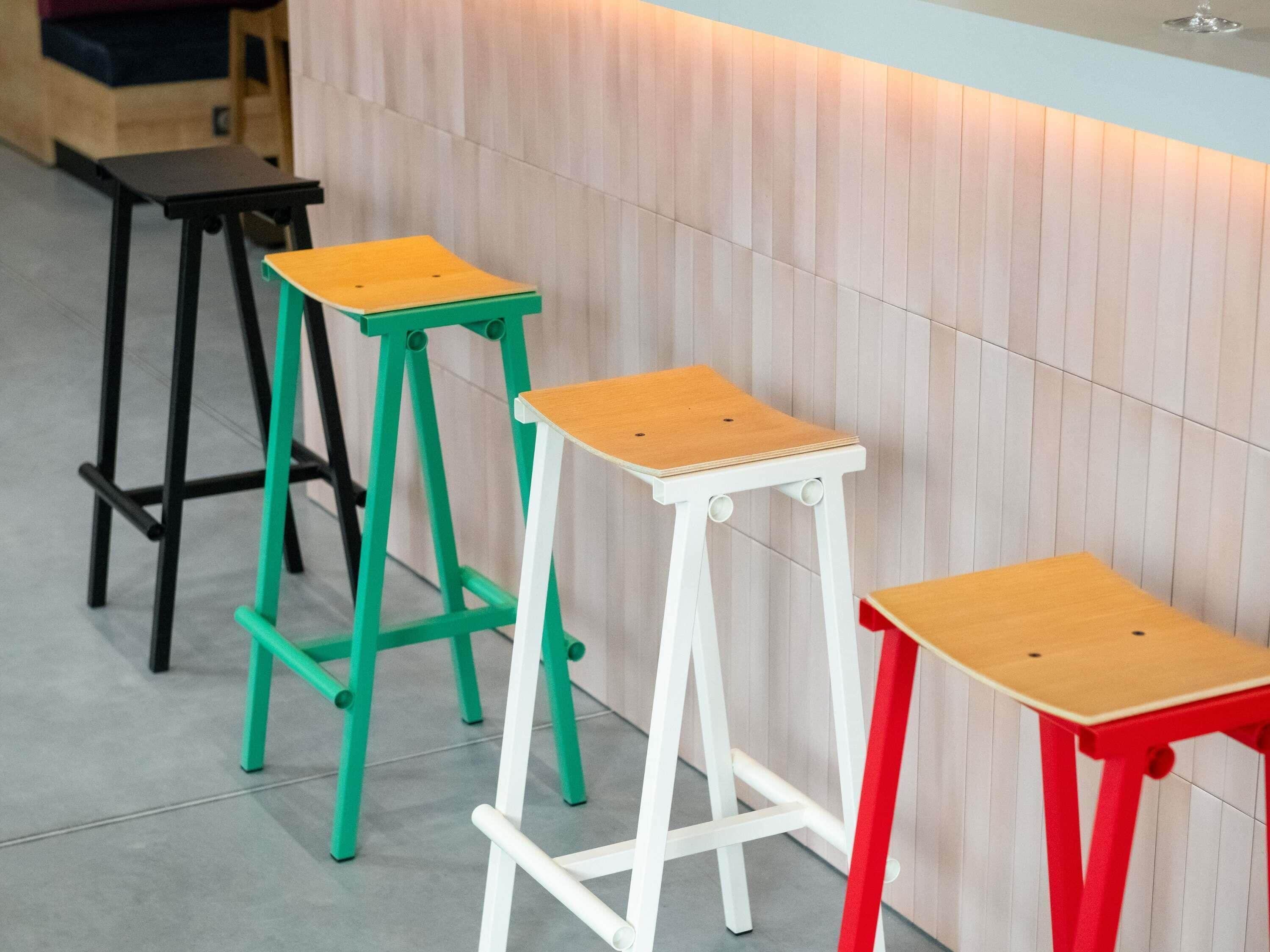 Tres taburetes con asientos de madera y patas de metal en varios colores.