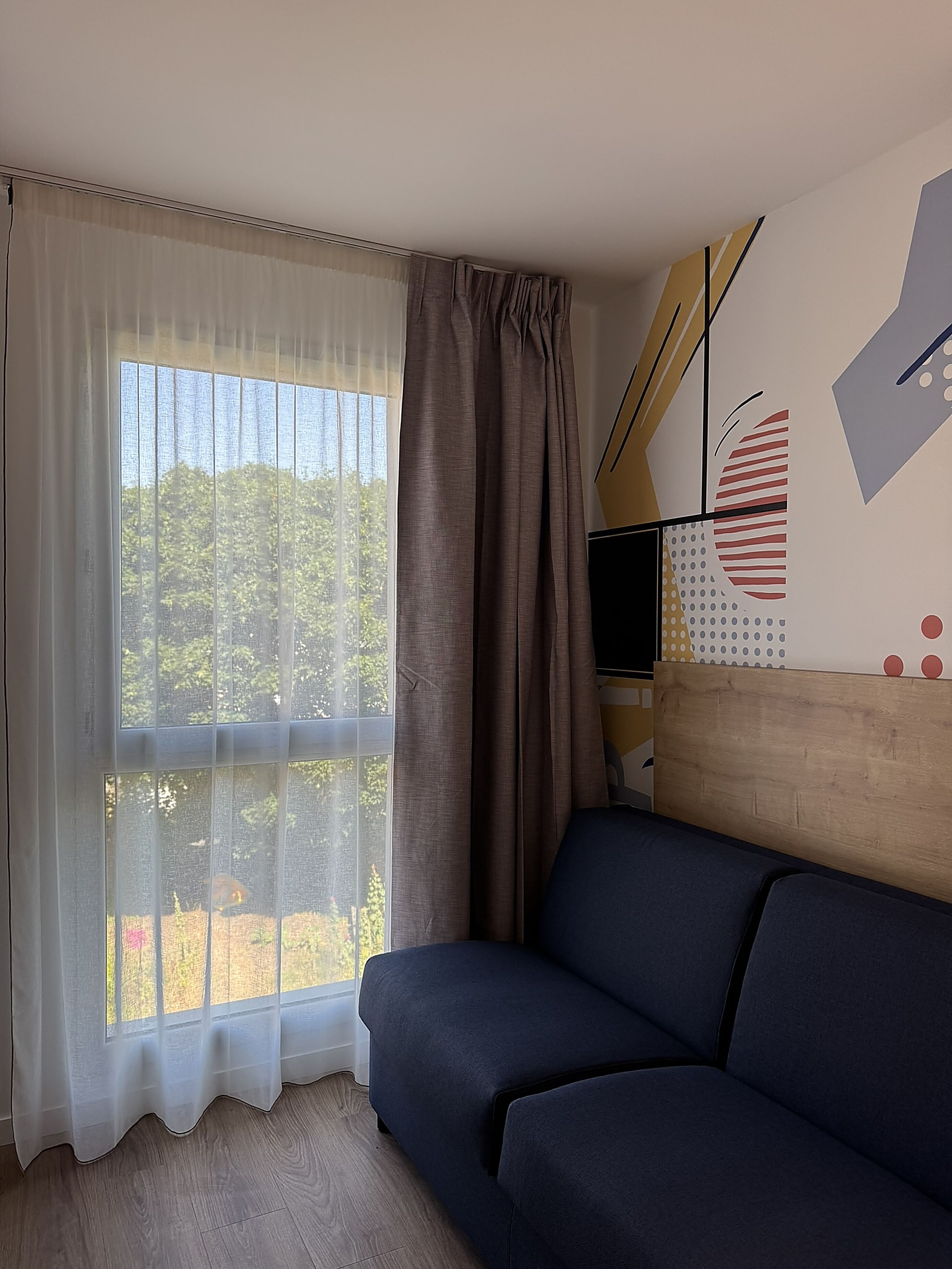 Una habitación con sofá, televisor, ventana con cortinas y una pared con diseño geométrico.