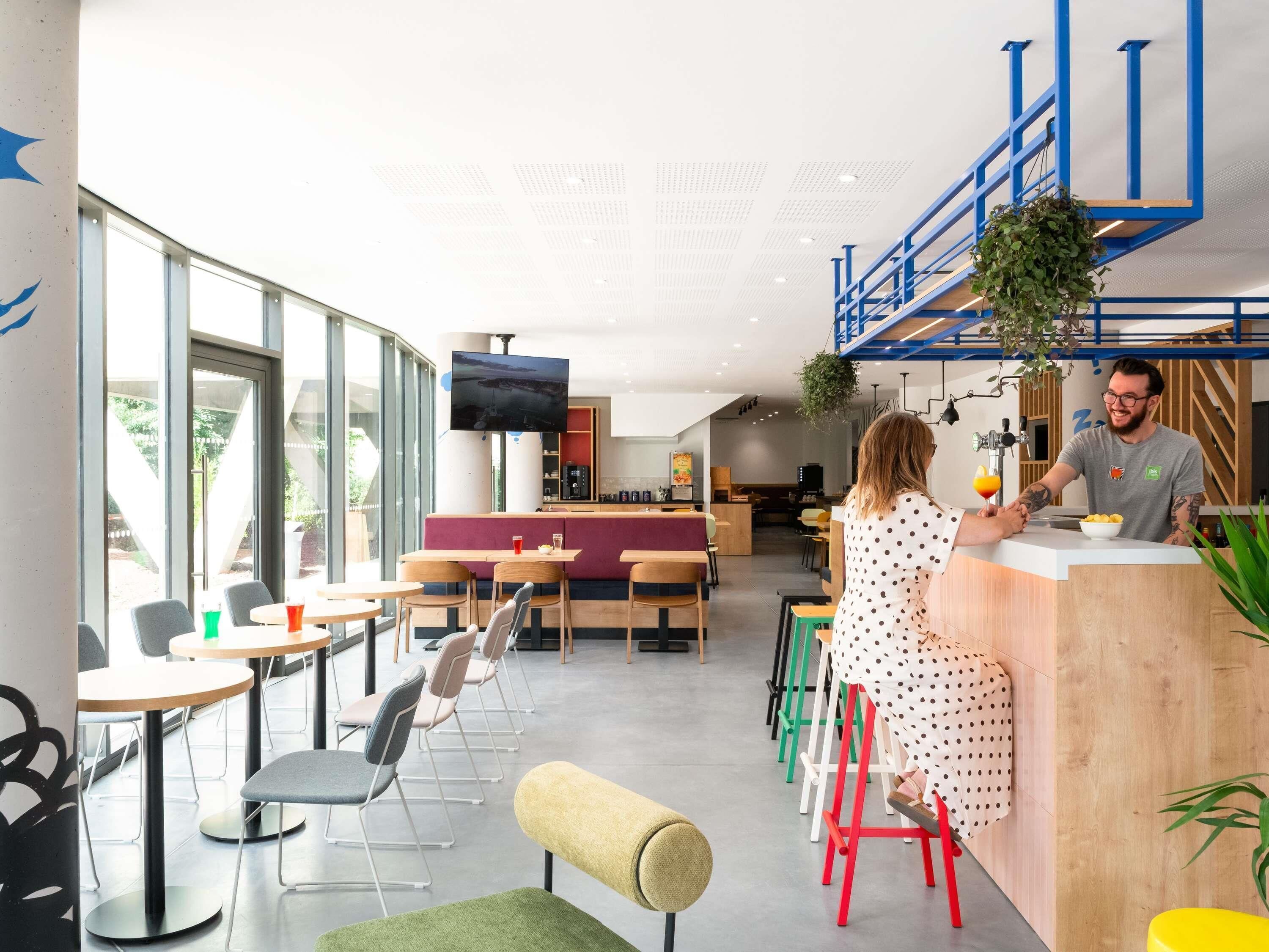 Un interior de cafetería moderna con barra, disposición de mesas y una pantalla de televisión.