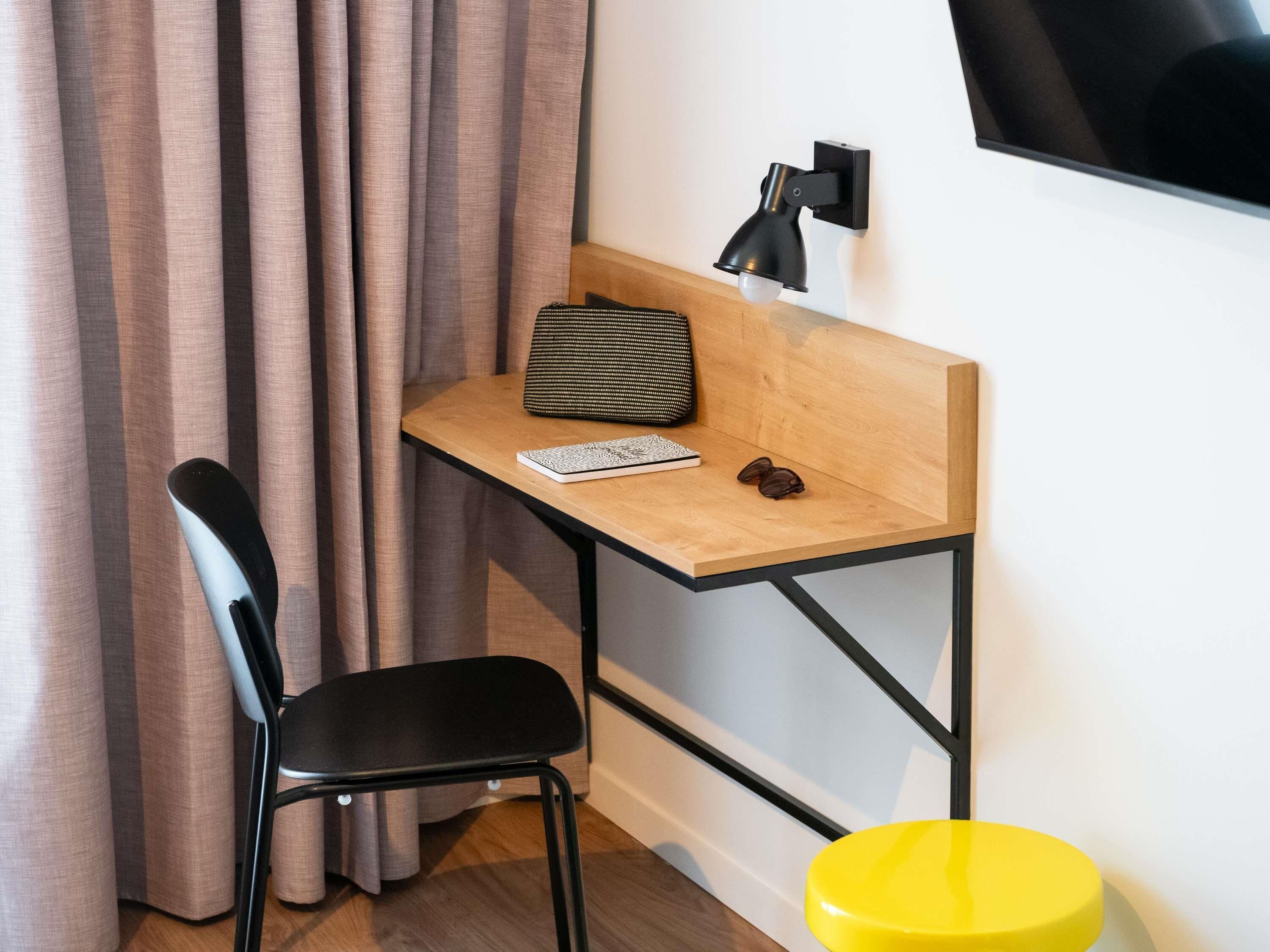 Un pequeño espacio de trabajo con escritorio, silla y lámpara fijada a la pared.