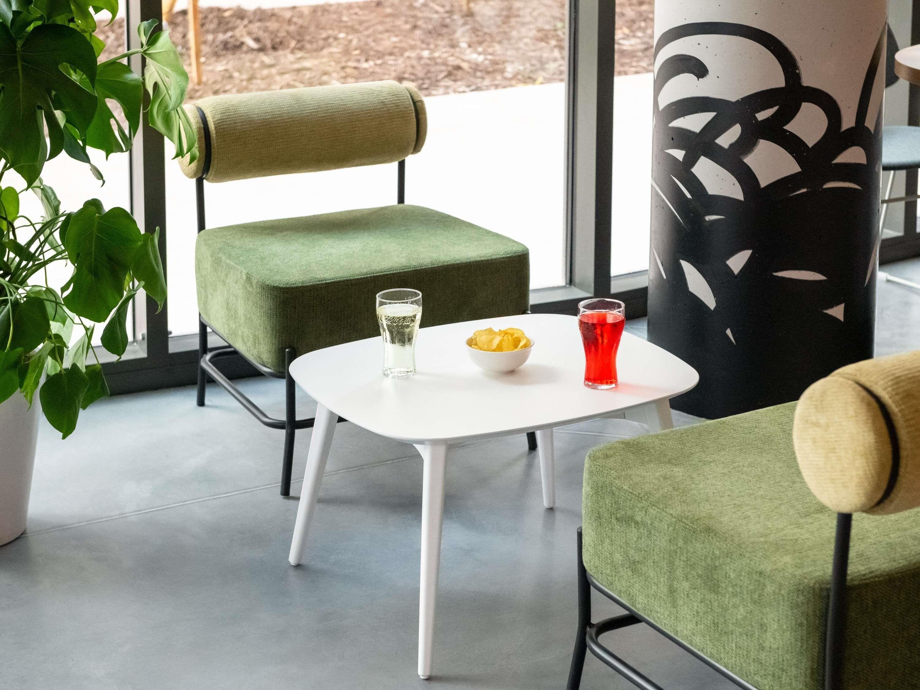 A modern indoor seating area with green upholstered chairs, a white table, and a glass of water.