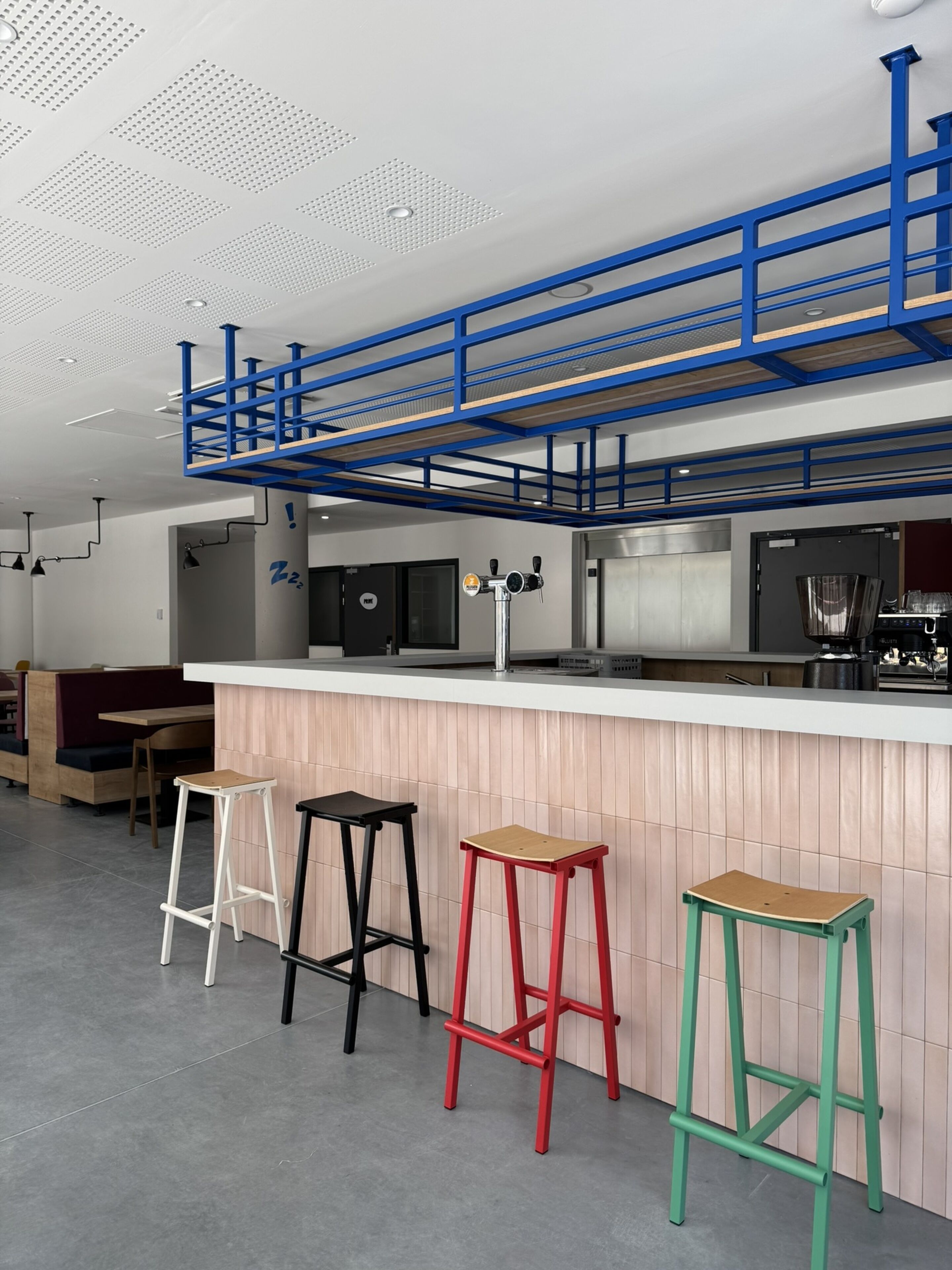 Zona de bar con taburetes, una barra y una estructura azul en el techo.