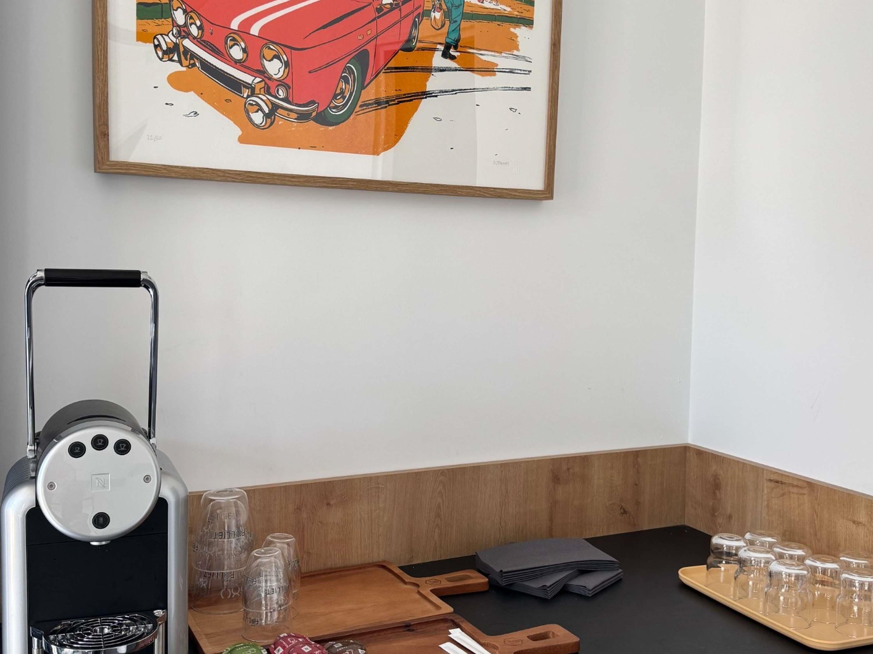 A room with a coffee machine, a framed artwork of a car, and a tray with cups and condiments.