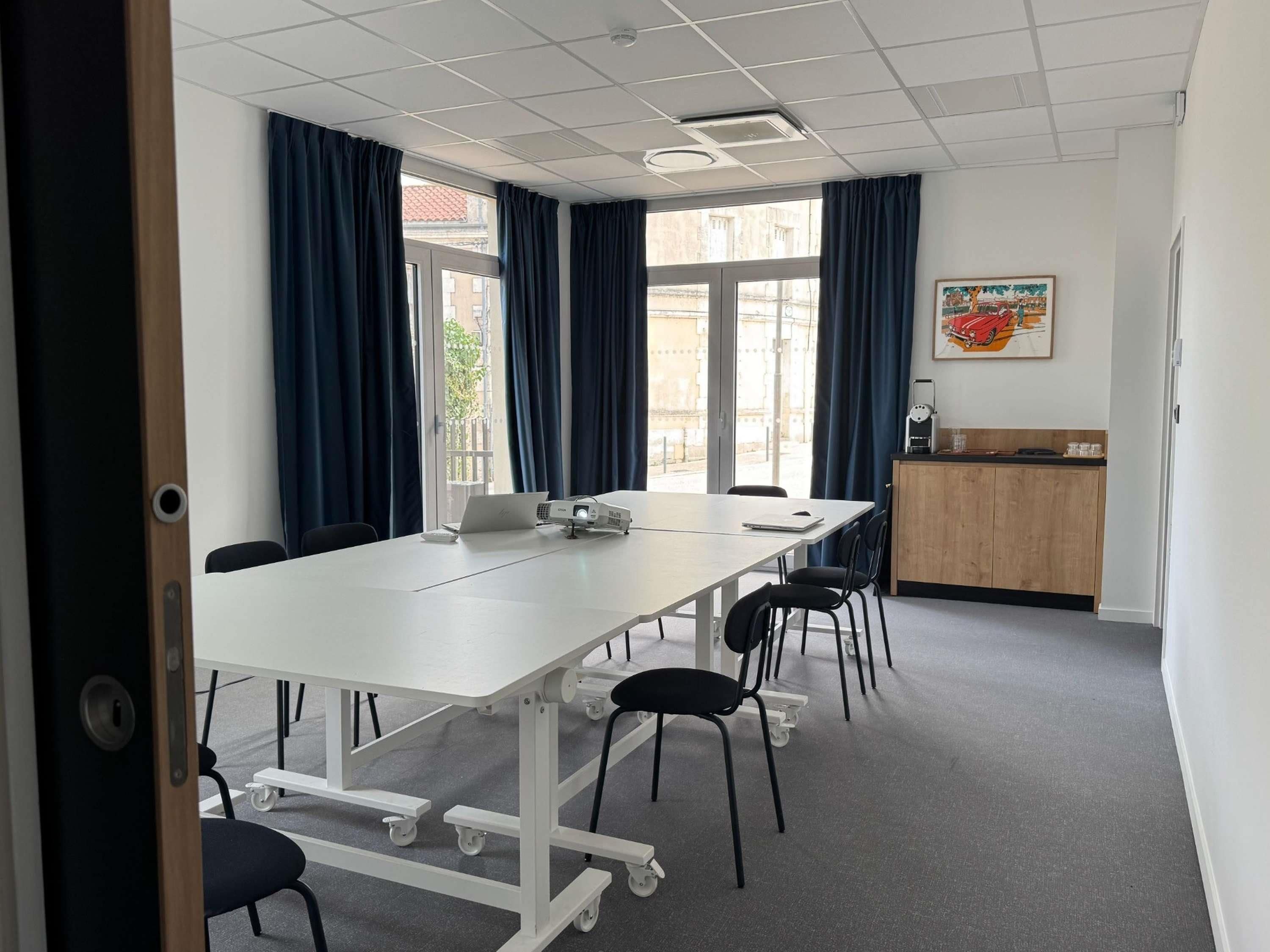 A conference room with a white table, black chairs, a projector, and a small kitchenette area.