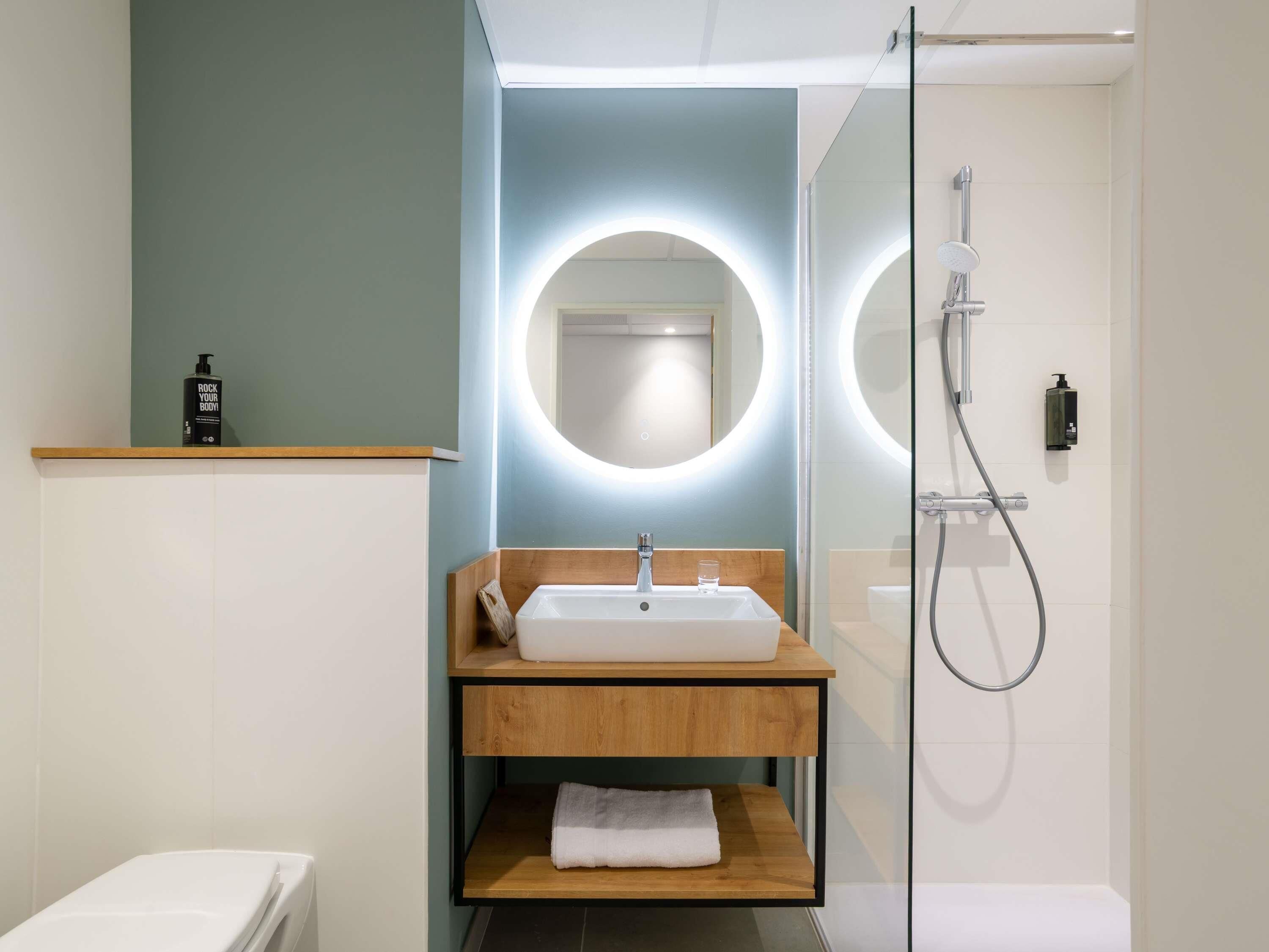 A modern bathroom with a white sink, wooden vanity, and a glass shower enclosure.