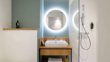 A modern bathroom with a white sink, wooden vanity, and a glass shower enclosure.