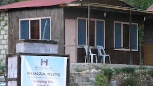 Un bâtiment rustique en bois, doté de nombreuses fenêtres, d’une enseigne publicitaire pour les « Hunza Huts » et d’un espace extérieur aménagé pour s’asseoir.