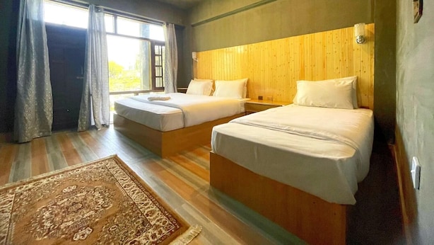 Une chambre d’hôtel avec deux lits, un ventilateur de plafond et une grande fenêtre avec des rideaux.