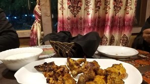 Une table à manger avec une assiette de viande grillée, un bol de sauce blanche et une chaise en osier.