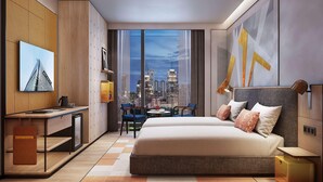 A modern hotel room with a bed, desk, and a cityscape view through large windows.